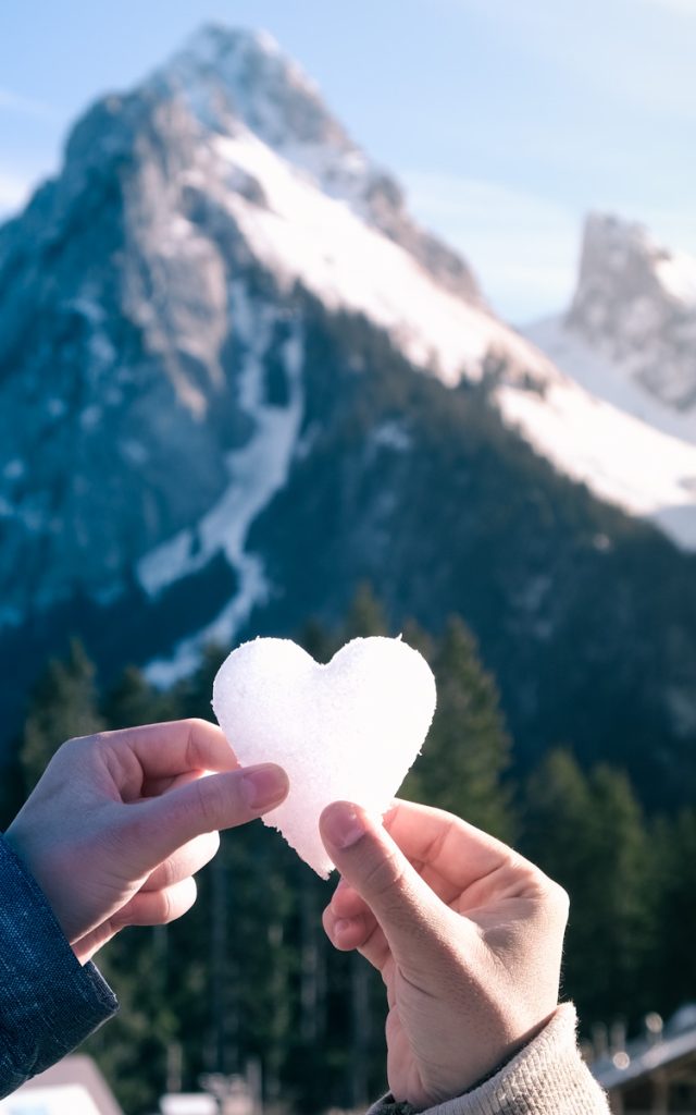 Deux mains tiennent un coeur en neige devant la Dent d'Oche