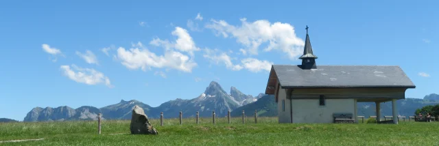 Chapelle de Champeillant tegen een blauwe lucht en groen gras. De top van de Dent d'Oche steekt af op de achtergrond.