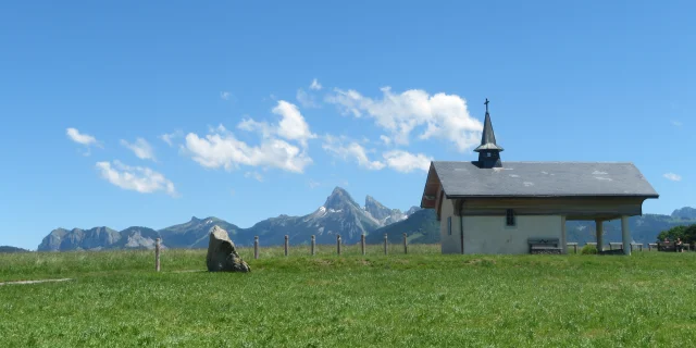 Chapelle de Champeillant against a blue sky and green grass. The Dent d'Oche peak stands out in the background.