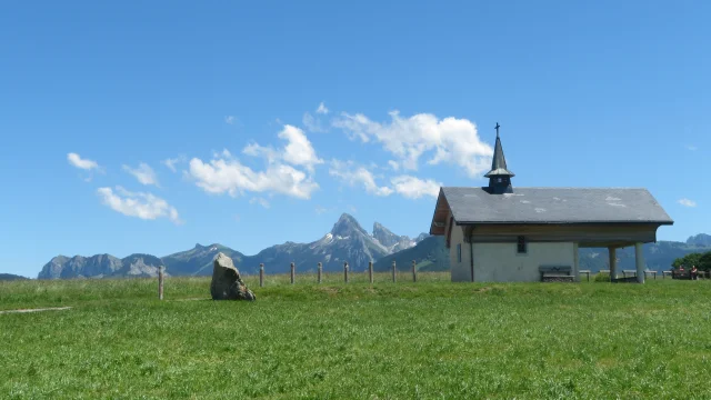 Chapelle de Champeillant sur un ciel bleu et une herbe verte. Le pic de la Dent d'Oche se détache dans le fond.