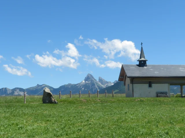 Chapelle de Champeillant against a blue sky and green grass. The Dent d'Oche peak stands out in the background.