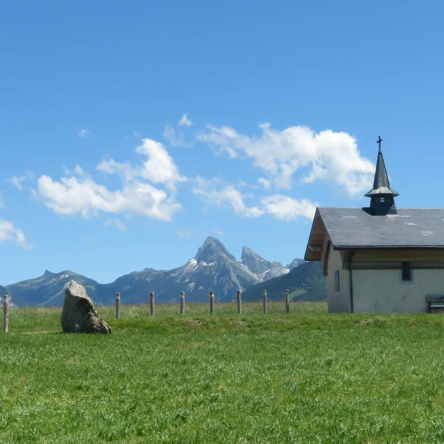 Chapelle de Champeillant tegen een blauwe lucht en groen gras. De top van de Dent d'Oche steekt af op de achtergrond.