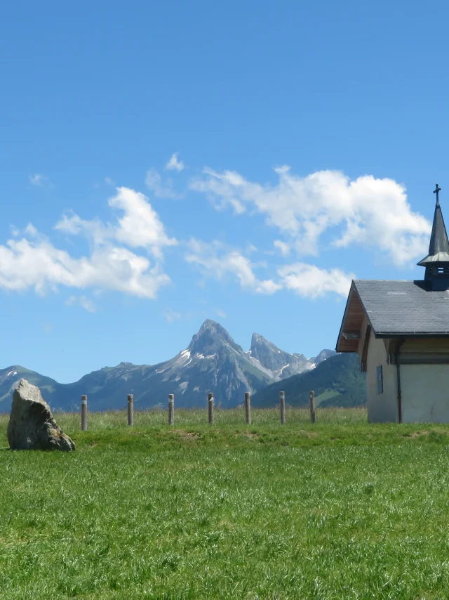 Chapelle de Champeillant tegen een blauwe lucht en groen gras. De top van de Dent d'Oche steekt af op de achtergrond.