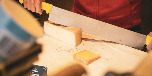 Une dame habillé en rouge qui coupe du fromage.