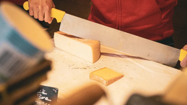 Une dame habillé en rouge qui coupe du fromage.