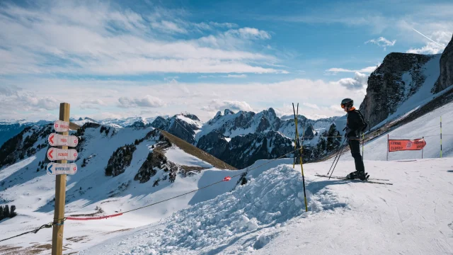 Haut Des Pistes De Ski Thollon Les Memises. A skier looks out over the landscape. In the background are snow-capped mountains and in the foreground a piste sign.