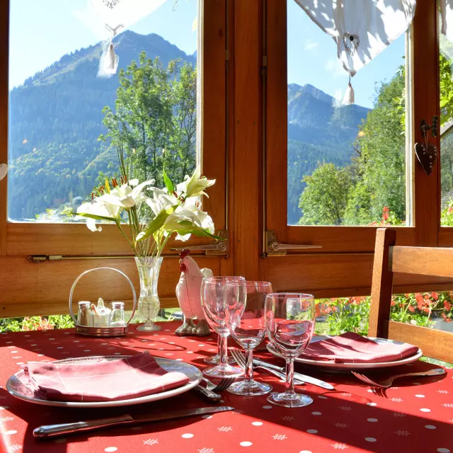 Table prête à servir un repas, nappe rouge, fleurs dans un vase et vue sur la montagne