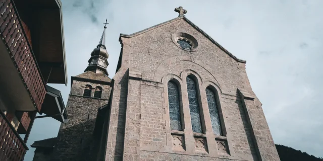 The Abbey of Abondance is located in the heart of the mountains. The photo shows the forecourt of the Abbey, with its huge grive stone façade and imposing stained-glass windows at the front.