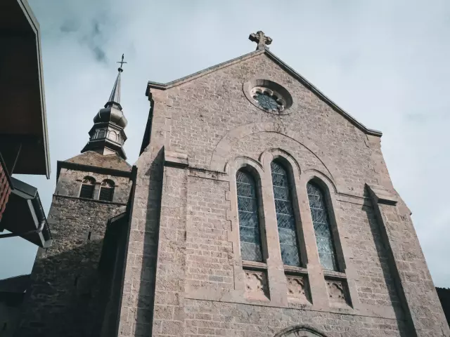 L’abbaye d’Abondance se situe au coeur des montagnes. La photo montre le parvis de l'Abbaye avec une immense façade en pierre grive et d'imposants vitraux sur le devant.