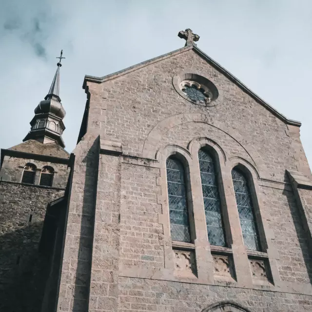 The Abbey of Abondance is located in the heart of the mountains. The photo shows the forecourt of the Abbey, with its huge grive stone façade and imposing stained-glass windows at the front.