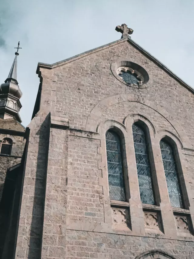 L’abbaye d’Abondance se situe au coeur des montagnes. La photo montre le parvis de l'Abbaye avec une immense façade en pierre grive et d'imposants vitraux sur le devant.