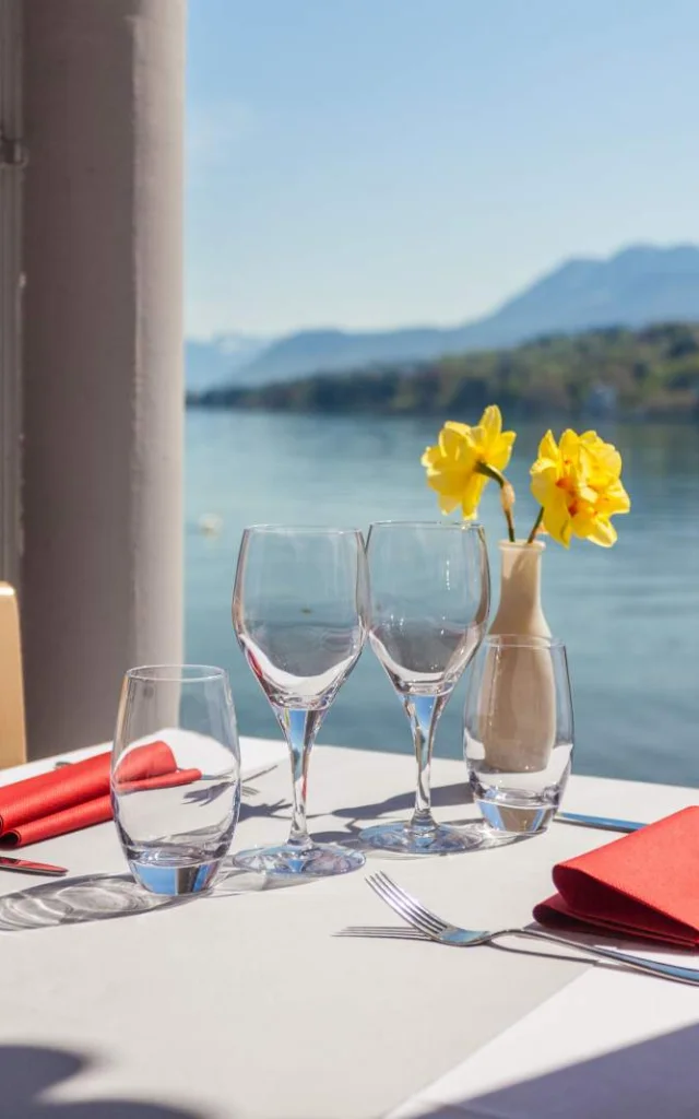 White tablecloth, lake view, two empty wine glasses and two yellow flowers in a vase