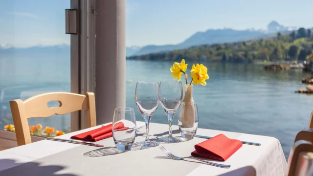 Table nappe blanche, vue sur le lac, deux verres de vin vides et deux fleurs jaunes dans un vase