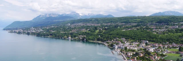 Lake and coast in the foreground. Buildings and trees can be seen from a drone view with the mountains in the background.