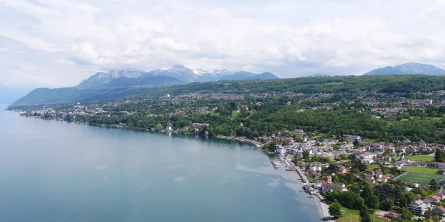 Meer en kust op de voorgrond. De gebouwen en bomen zijn te zien vanuit een drone-view met de bergen op de achtergrond.