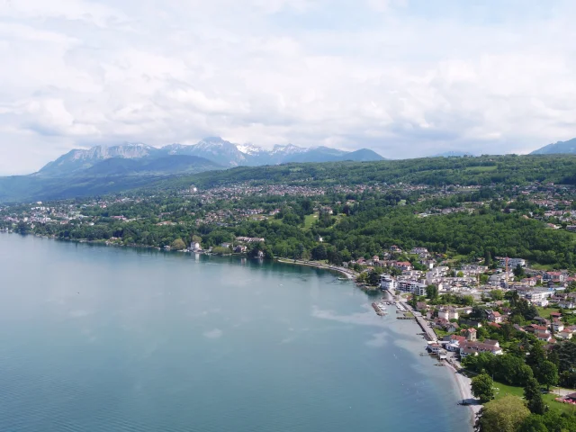 Lake and coast in the foreground. Buildings and trees can be seen from a drone view with the mountains in the background.