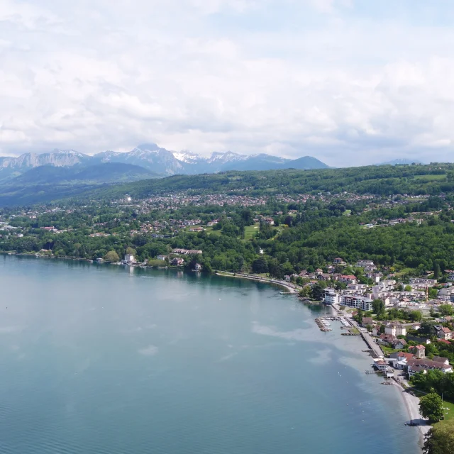 Meer en kust op de voorgrond. De gebouwen en bomen zijn te zien vanuit een drone-view met de bergen op de achtergrond.