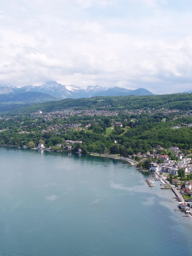 Meer en kust op de voorgrond. De gebouwen en bomen zijn te zien vanuit een drone-view met de bergen op de achtergrond.