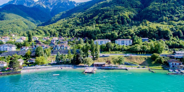 Vue drône depuis le lac. L'eau est bleu et on voit la montagne en fond avec le port.