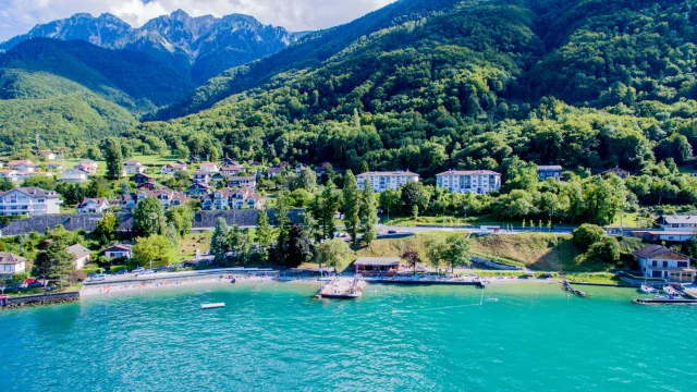 Vue drône depuis le lac. L'eau est bleu et on voit la montagne en fond avec le port.