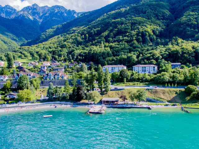 Vue drône depuis le lac. L'eau est bleu et on voit la montagne en fond avec le port.