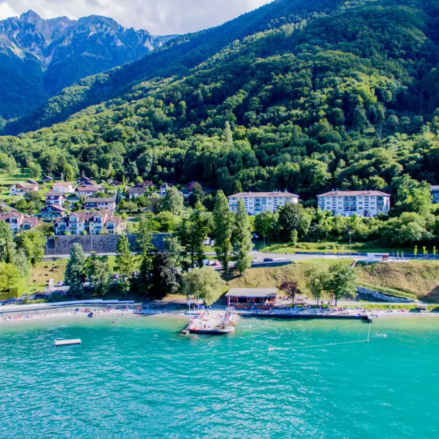 Vue drône depuis le lac. L'eau est bleu et on voit la montagne en fond avec le port.