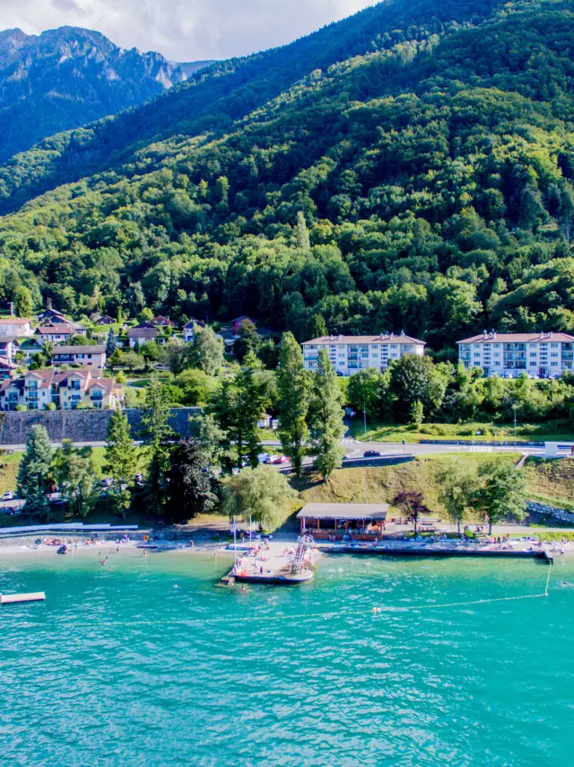 Vue drône depuis le lac. L'eau est bleu et on voit la montagne en fond avec le port.