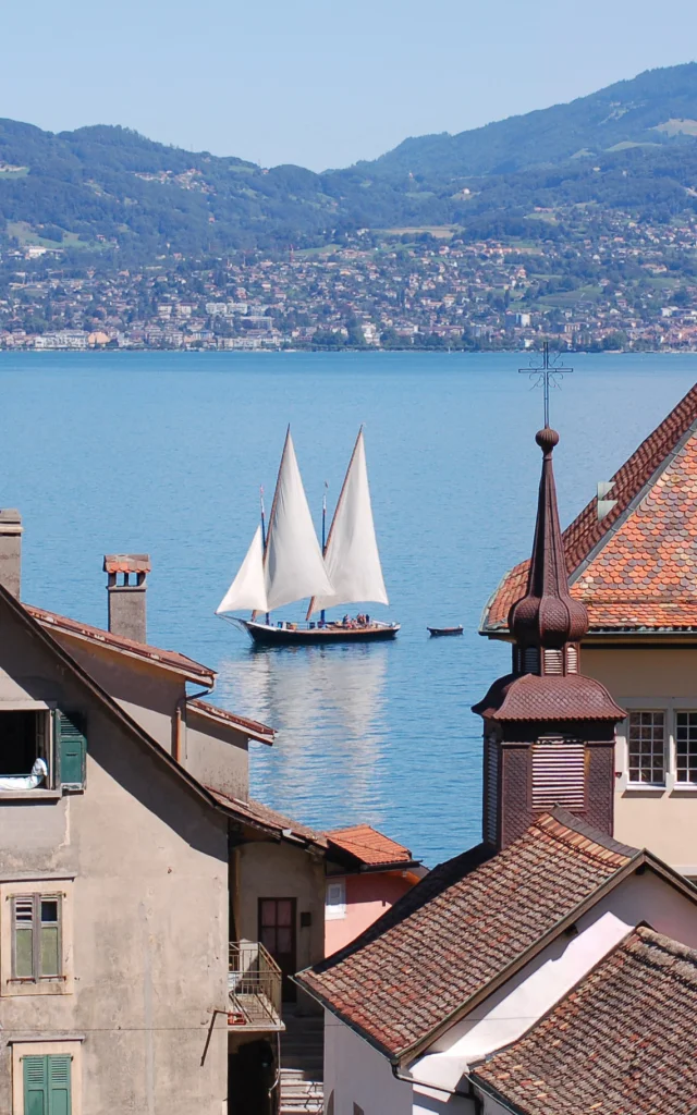 View of the lake, with a sailboat on the water and the buildings of St Gingolph in the foreground.