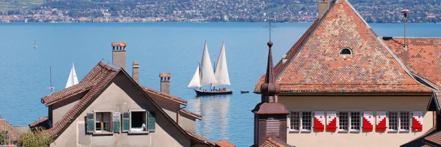 Vue sur le lac, on voit un voilier sur l'eau et les bâtiments de St Gingolph en premier plan