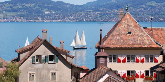 View of the lake, with a sailboat on the water and the buildings of St Gingolph in the foreground.