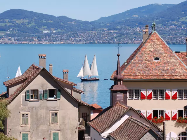 Vue sur le lac, on voit un voilier sur l'eau et les bâtiments de St Gingolph en premier plan