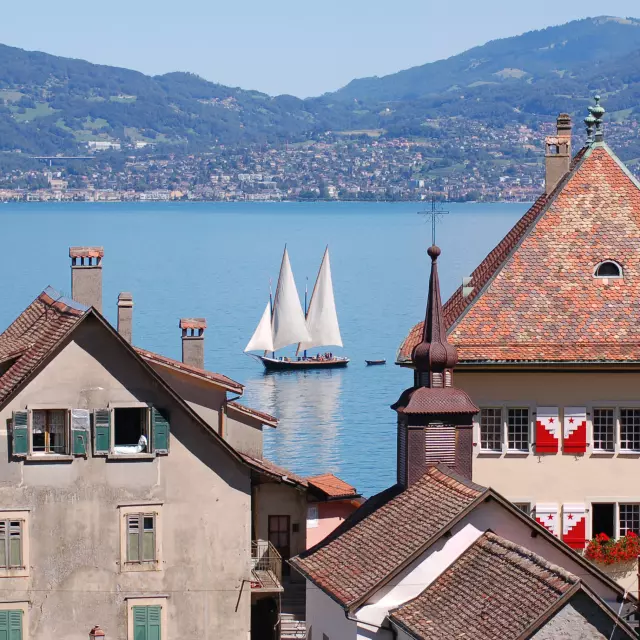 Vue sur le lac, on voit un voilier sur l'eau et les bâtiments de St Gingolph en premier plan