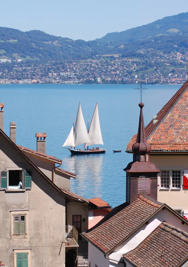 View of the lake, with a sailboat on the water and the buildings of St Gingolph in the foreground.